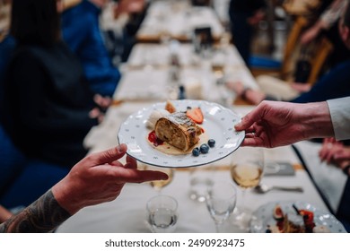 Riga, Latvia March 20, 2024 - A waiter serves a dessert plate with apple strudel, ice cream, and berries at a restaurant, with a blurred background of diners. - Powered by Shutterstock