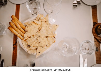 Riga, Latvia March 20, 2024 - Top view of a table setting with a basket of flatbread and breadsticks, surrounded by wine glasses and cutlery. Copy space. - Powered by Shutterstock