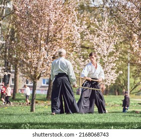 Riga, Latvia - May 8, 2022: Two aikido fighters training with stick in the public park. Blooming sakura at the background.
