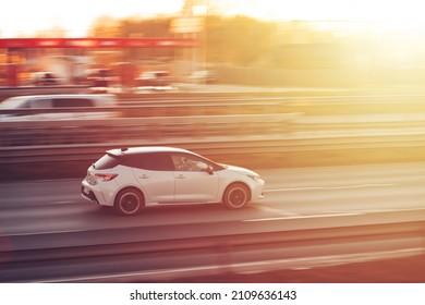 Riga, Latvia - November 12, 2021: White Toyota Corolla Hybrid Hatchback drives on a highway on a sunny evening, golden hour