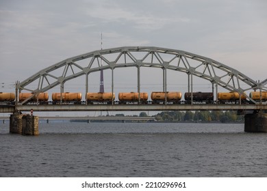 Riga railway bridge over the Daugava River with iron arch and oil tank wagons travelling over the bridge and Riga radio and tv tower in the background