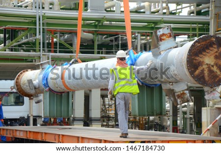 Rigger construction worker holding control a primary transfer line of heat exchanger which its connecting to the load while crane is lifting construction site or chemical plant.
