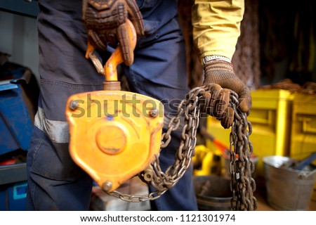 Rigger high risk worker wearing heavy duty CS5 hand protection glove, doing checking inspection a heavy duty 3 tones yellow lifting chains block prior used on construction site Perth city, Australia 