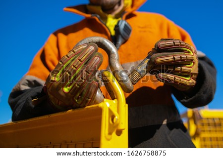 Rigger high risk worker wearing safety heavy duty glove, inserting pin into D- shape shackle which its connecting on  crane lifting lug gate hook prior lift at construction site Perth city