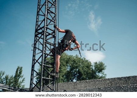Rigger technician hanging upside down, maintaining and installing equipment on a tall metal truss structure outdoors