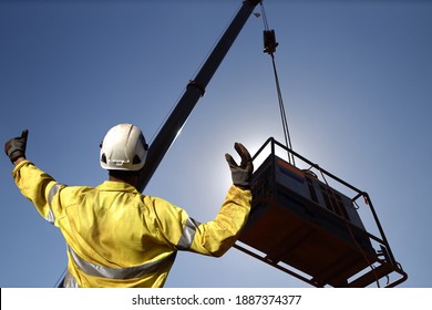 Rigger wearing a glove standing raising using a hand signal by moving finger slowly to directing communication with crane driver to move the boom up at construction site, Sydney, Australia   