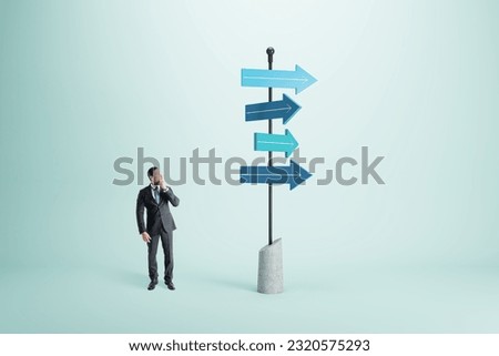 Right choice, dilemma and business strategy direction concept with pensive man in black suit looking at signpost with blue arrows in different direction on abstract light background