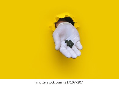 A Right Doctor's Hand In A White Medical Glove Holds A Handful Of Activated Carbon Tablets. Torn Hole In Yellow Paper. Indigestion Treatment Concept. Copy Space.