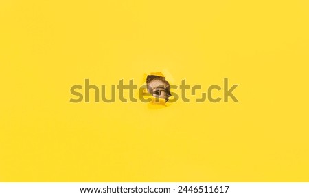 A right eye looking through a hole in a yellow paper. Voyeurism. The man is watching the wife. A curious look. Jealousy, spying on or overhearing the concept. Copy space. Stock fotó © 