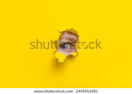 The right eye looks into a hole in the yellow paper. The child watches his parents. A curious look. Jealousy, eavesdropping concept. Copy space. Stock fotó © 