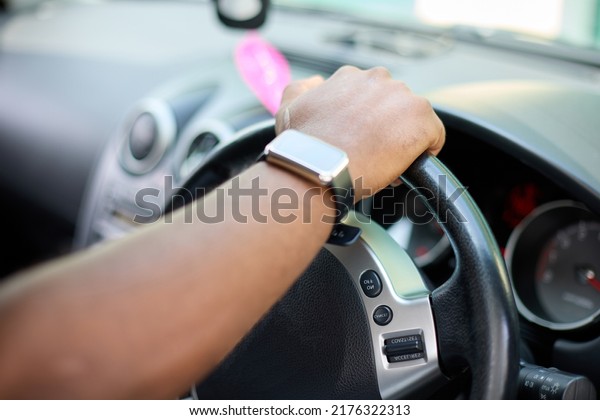 The right\
hand of a black man on the steering wheel of a car. An African man\
in a smart watch drives a\
vehicle