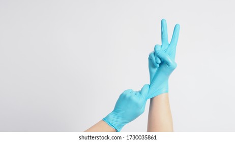 Right Hand Is Doing A Good Luck Sign.It Is Hand Gesturing Two Finger With Blue Gloves And Left Hand Is Pulling On White Background.