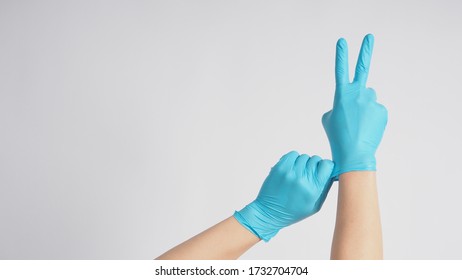 Right Hand Is Doing A Good Luck Sign.It Is Hand Gesturing Two Finger With Blue Gloves And Left Hand Is Pulling On White Background.