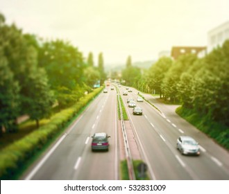 Right Hand Driving Motorway With Speedy Cars Surrounded By Green Backgrounds - Tilt Shift Lens Used To Accent Motorway And To Emphasize The Speed Vision