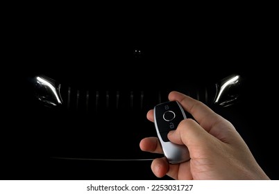 right hand holding car remote key to unlock a black sports car with background of led headlight and stainless grille park in the dark garage - Shutterstock ID 2253031727