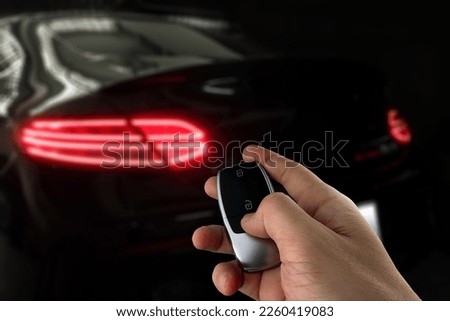 right hand is holding a car remote key to unlock and lock luxury black sports car with background of nice led tail light park in the dark garage mercedes benz c200 coupe