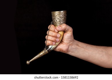 right hand of a man holds a souvenir horn for alcoholic drinks on a black background. The edges of the horns inlaid with metal