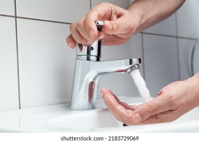The right hand opens the tap on the lever faucet above the white tiled sink. A jet of water pours on the left hand. White tiles on the wall - Shutterstock ID 2183729069