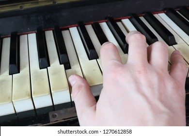 A right hand playing a E (MI) major chord on an old black piano with yellowed cracked keys, pressing the E (MI), G# diesis (SOL#), B (SI) notes