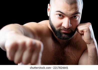 Right Hook! Close Up Portrait Of Strong Confident Shirtless Man With Beard Keeping Fists Against Black Background.