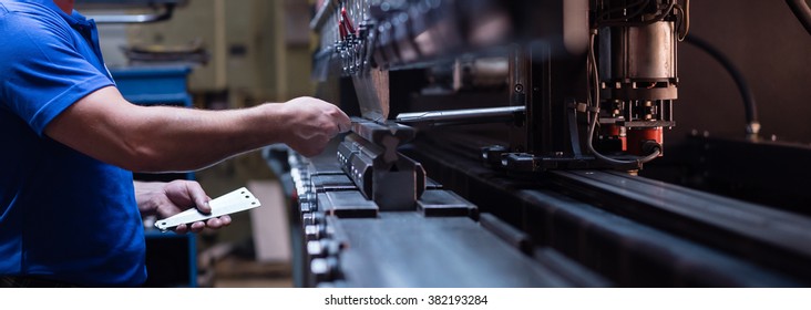 right side close-up of a worker holding a metal plate against a manufacturing machinery, in the right hand, and several other metal plates in his left hand - Shutterstock ID 382193284