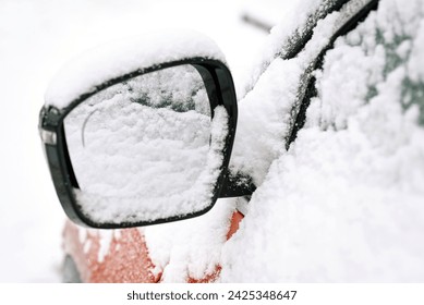 Right side mirror of a parked car. Snow covered car mirror closeup, selective focus. Snowy vehicle on parking lot in winter day. 