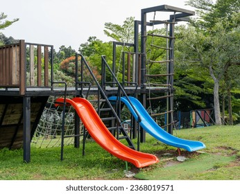 Right side view of two children slides, red and blue, and climbers attached to a steel and wooden platform that makes an outdoor jungle gym. - Powered by Shutterstock