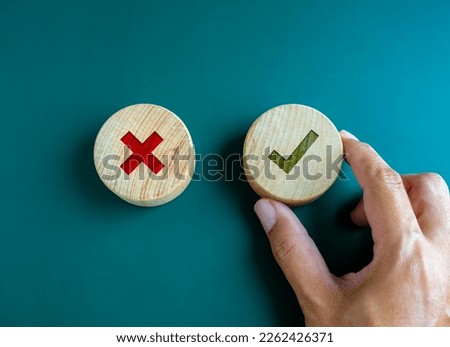 Right and wrong. Close-up green check mark and red X mark icon on round wooden button, chosen green check mark by business's hand. Picking correct sign. Approving, voting or right decision concepts.