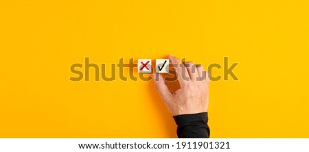 Right and wrong icons on wooden cubes with male hand choosing the right icon on yellow background. Approving, voting or right decision concept.