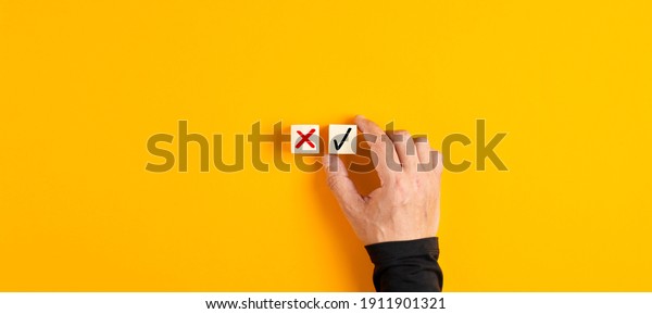 Right and wrong icons on wooden cubes with\
male hand choosing the right icon on yellow background. Approving,\
voting or right decision\
concept.\
\
