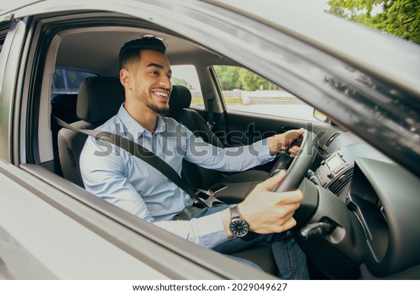 Right-hand drive\
auto concept. Positive middle-eastern guy in formal outfit going to\
office, driving car, happy arab businessman enjoying his new luxury\
automobile, shot from\
outside
