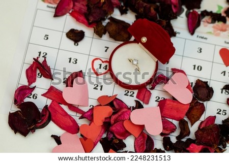The ring box is placed on the calendar together with many flower petals, and Valentine's Day is marked on the calendar in red. Marriage proposal on Valentine's Day