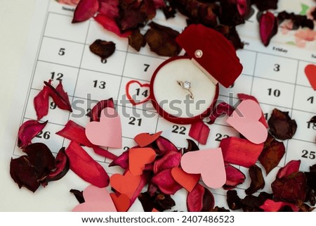 The ring box is placed on the calendar together with many flower petals, and Valentine's Day is marked on the calendar in red. Marriage proposal on Va