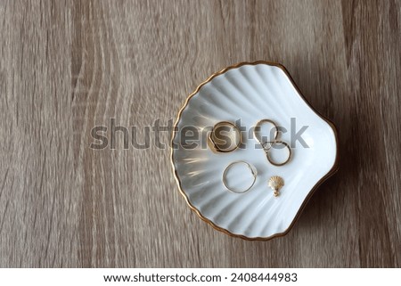 Ring dish shaped like a seashell with gold rings, earrings and pendant. Wooden background, top view.