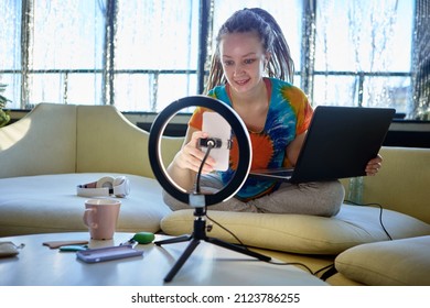 Ring light with mobile phone holder used by beauty blogger during makeup classes inside.