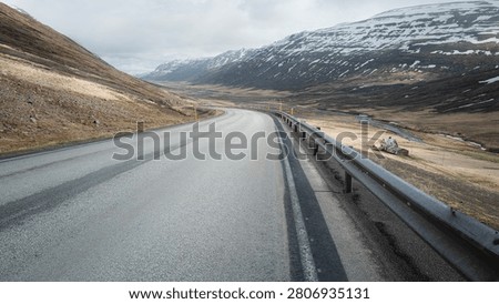 The Ring Road sweeps through a broad North Iceland valley, snow-dusted peaks rising on both sides above an abandoned turf farmhouse in soft spring light.