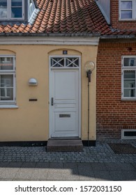 Ringkobing Jutland Denmark August 14th 2019 - Facade Of A Old Yellow House With White Front Door And White Wooden Window And The Next Door Neighbour Window On A Brick Wall In A Sunny Summer Afternoon