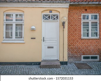 Ringkobing Jutland Denmark August 14th 2019 - Facade Of A Old Yellow House With White Front Door And White Wooden Window And The Next Door Neighbour Window On A Brick Wall In A Sunny Summer Afternoon