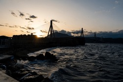 Rio Antirio Bridge In Patras At The Sunset On A Beautiful Evening With Waves At The Dock Of Rio.