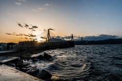 Rio Antirio Bridge In Patras At The Sunset On A Beautiful Evening With Waves At The Dock Of Rio.