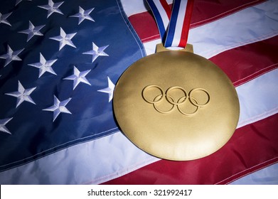 RIO DE JANEIRO, BRAZIL - FEBRUARY 3, 2015: Large gold medal featuring Olympic rings sits on American flag background.