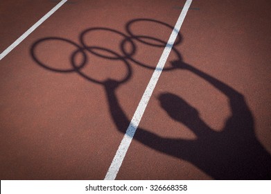 RIO DE JANEIRO, BRAZIL - FEBRUARY 12, 2015: Shadow Of An Athlete Holds Olympic Rings On The Lanes Of A Red Running Track. 