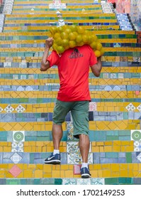 RIO DE JANEIRO, BRAZIL - JANUARY 3, 2020:  A worker carries a sack of oranges during the early morning on the famous Escadaria Selaron (Selaron  Stairway) in the historic center of Rio de Janeiro.  - Shutterstock ID 1702149253