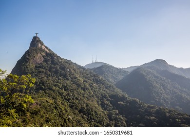 Rio De Janeiro, Brazil - July 4th 2016: Christ The Redeemer (Cristo Redentor) On Mount Corcovado During The Daytime With Clear Blue Sky Overhead & Mountains & Forest Trees Surrounding Everything