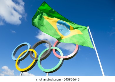 Rio de Janeiro, Brazil  - OCTOBER 14, 2015: Brazilian flag flies next to the Olympic rings standing under bright blue sky in the Queen Elizabeth Olympic Park. [illustrative editorial]