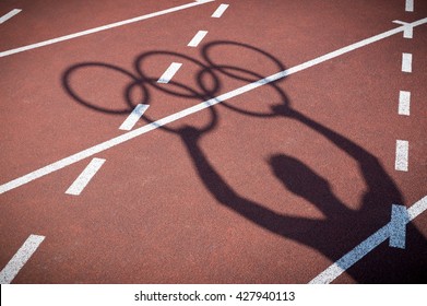 RIO DE JANEIRO - FEBRUARY 12, 2015: Shadow of an athlete holds Olympic rings on the lanes of a red running track.