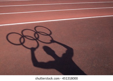 RIO DE JANEIRO - FEBRUARY 12, 2016: Shadow Of An Athlete Holds Olympic Rings On The Lanes Of A Red Running Track In Celebration Of The Summer Games.