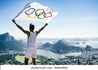 RIO DE JANEIRO - MARCH 21, 2016: Athlete stands holding Olympic flag above a city skyline view of Corcovado Mountain and Zona Sul.