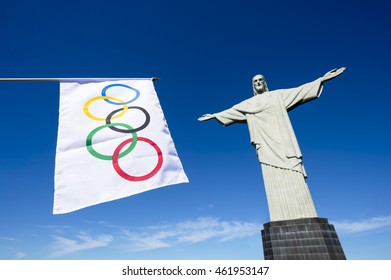 RIO DE JANEIRO - MARCH 21, 2016: Olympic flag hangs in clear blue sky next to the statue of Christ the Redeemer in celebration of the city hosting the Summer Games.