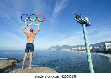 RIO DE JANEIRO - MARCH 27, 2016: Swimmer athlete holds Olympic rings standing  on a rock at Arpoador overlooking Ipanema Beach.